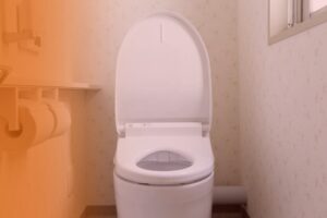A modern white toilet with an open lid stands against patterned wallpaper in a softly lit bathroom, next to rolls of toilet paper on the left.