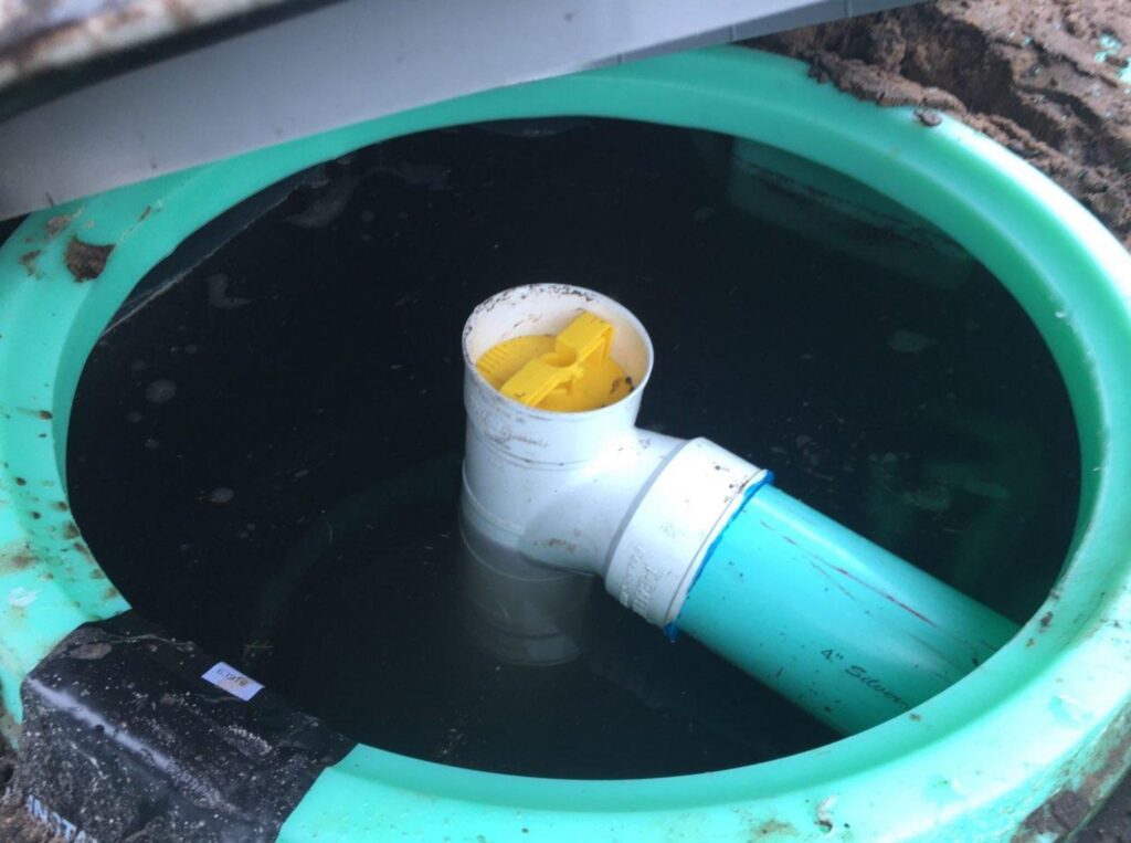 An open green septic tank riser reveals a yellow effluent filter installed inside a PVC pipe assembly above dark wastewater.