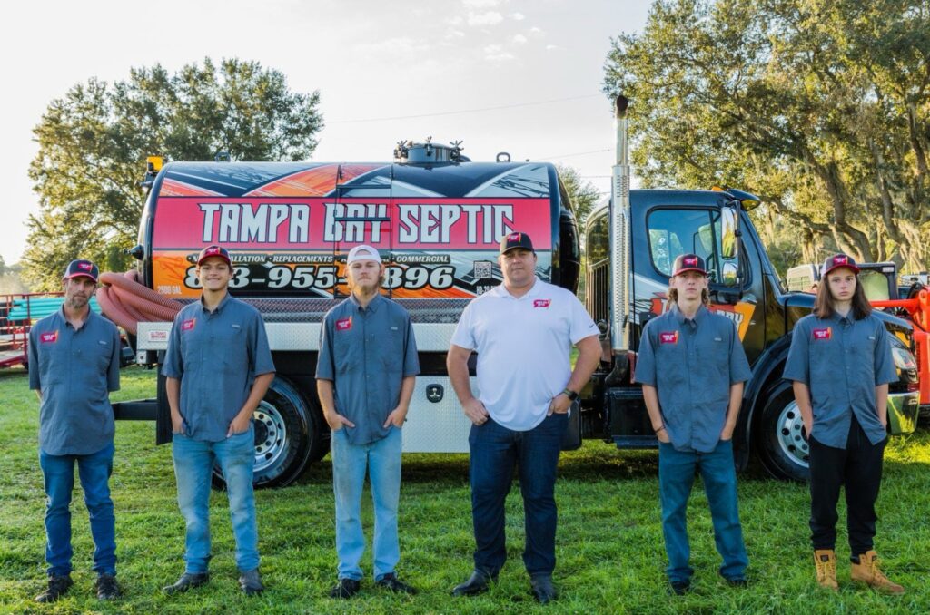 A professional team of technicians posing in front of a branded Tampa Bay Septic service truck.