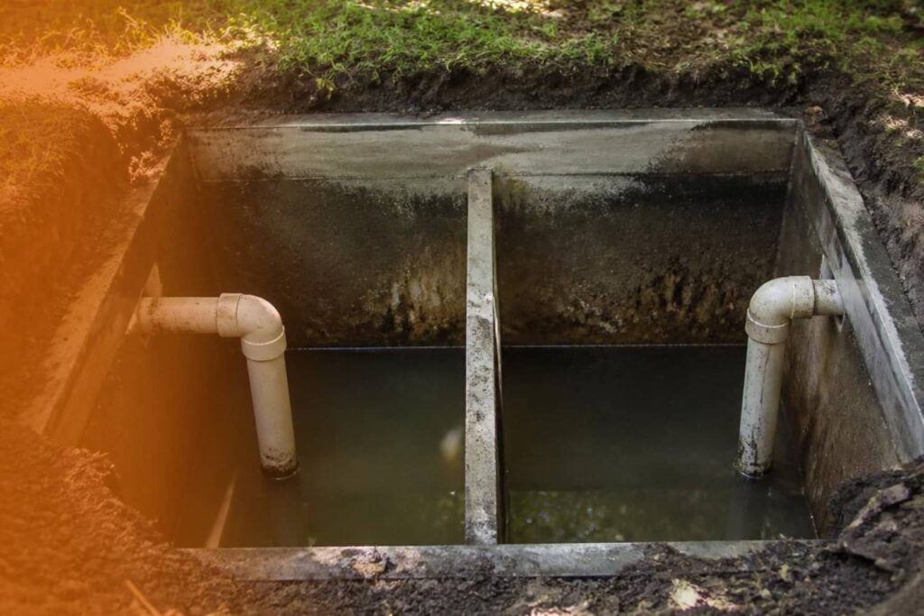 An open concrete septic tank divided into two chambers with white PVC pipe baffles extending into wastewater.
