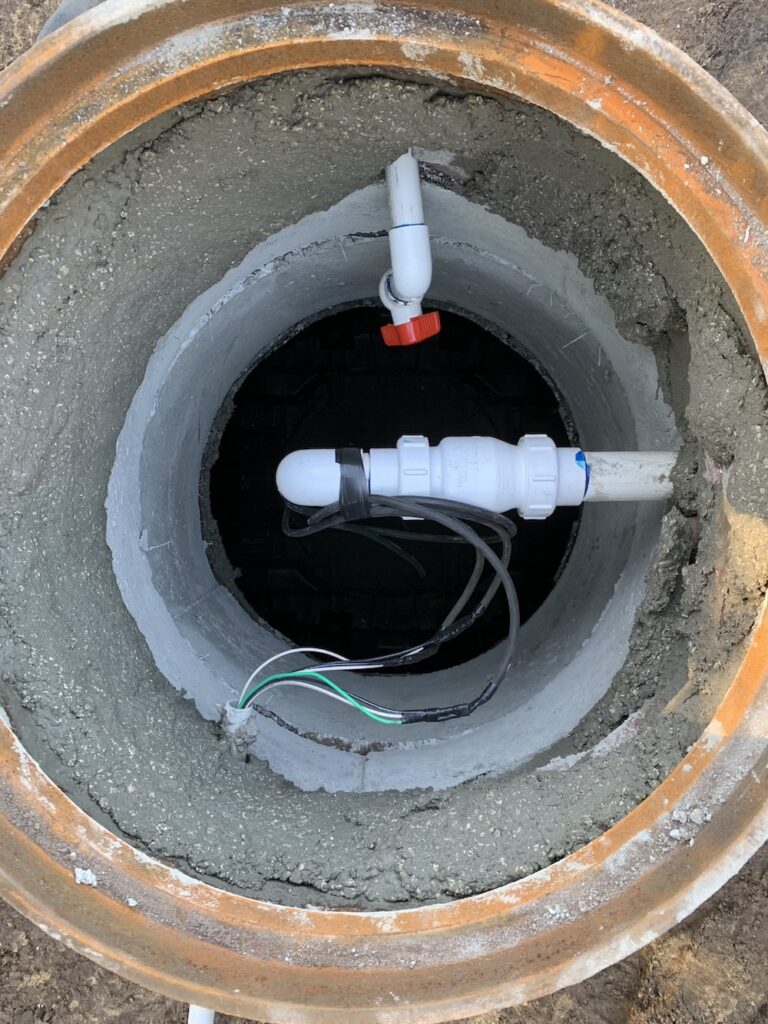 An overhead view looking into an open concrete septic tank riser with PVC piping and electrical wiring, highlighting essential components checked during a septic tank pumping lakeland fl system inspection.