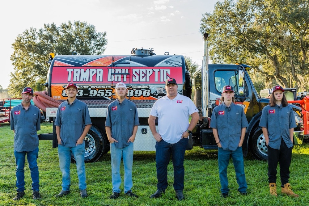 Six crew members from Tampa Bay Septic stand in uniform in front of a branded commercial service truck on a grassy field.