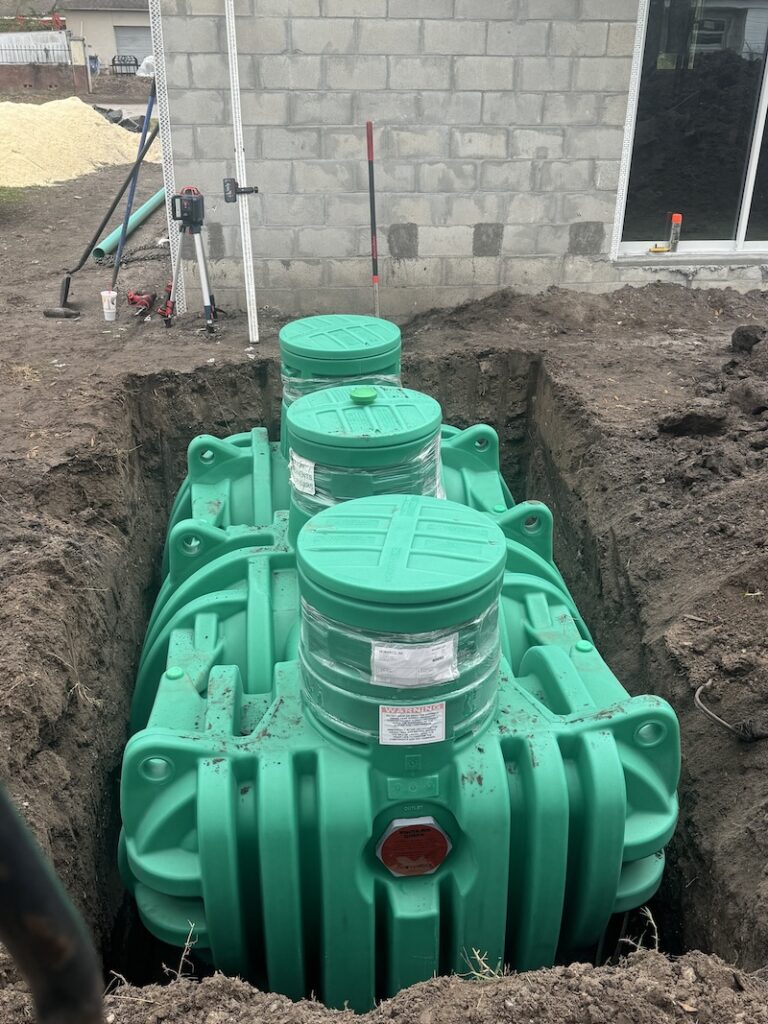 A newly installed green plastic septic tank system sits in an excavated trench next to a block building under construction, demonstrating a professional septic pumping lutz fl installation.