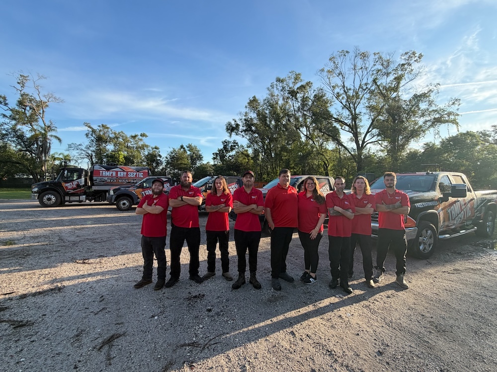A team of nine employees in matching red shirts stands in front of Tampa Bay Septic service vehicles specializing in septic tank installation Tampa FL.